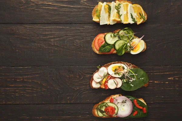 Variety of healthy vegetarian sandwiches on dark wood, top view — Stock Photo, Image