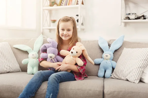 Happy little female child abraçando seus coelhos de brinquedo no sofá em casa — Fotografia de Stock