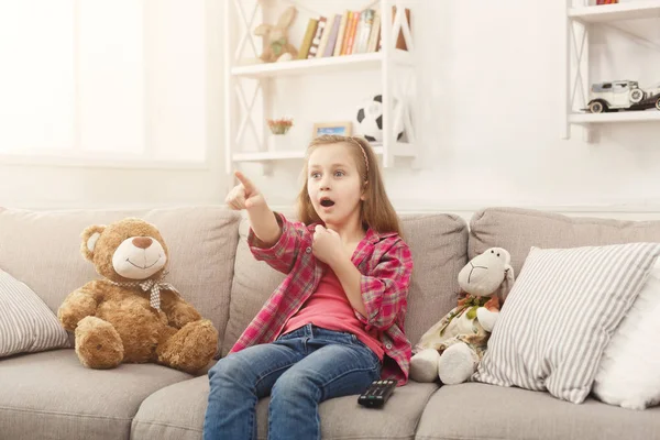 Skrämde casual liten flicka tittar på tv medan du sitter på soffan hemma — Stockfoto