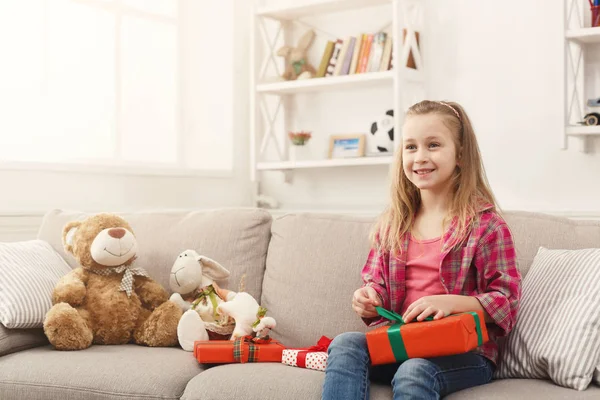Krásná malá holka upwrapping představuje na gauči doma — Stock fotografie