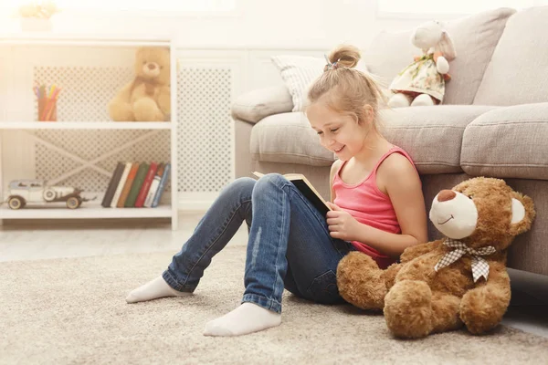 Šťastný malá holčička a její medvídek čtení knihy o podlahu doma — Stock fotografie