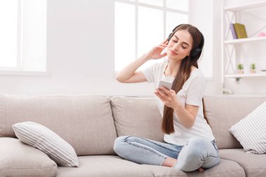 Cep telefonu ve bej kanepe kulaklıktan olan kadın