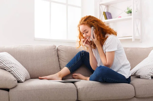 Young smiling beautiful woman using phone and tablet on sofa — Stock Photo, Image