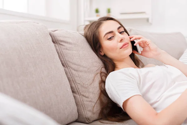 Chica joven hablando en el móvil tumbado en el sofá beige — Foto de Stock