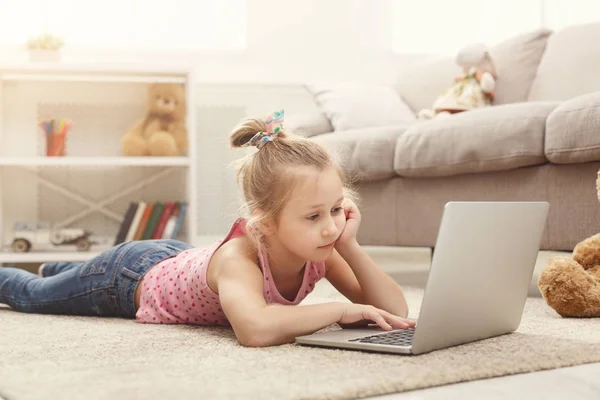 Petite fille mignonne faisant ses devoirs sur un ordinateur portable, assise sur le sol à la maison — Photo