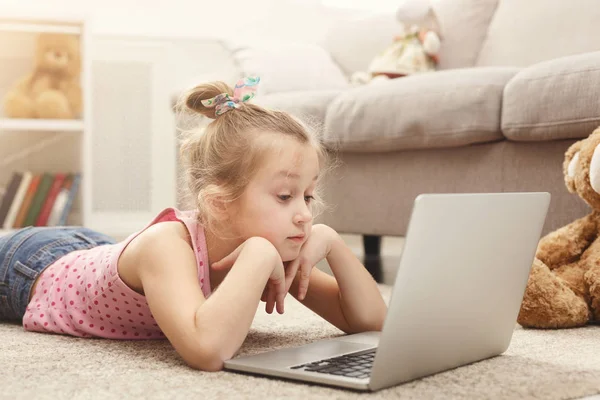 Ładna dziewczynka odrabiania lekcji na laptopie, siedząc na podłodze w domu — Zdjęcie stockowe