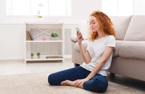 Chica pelirroja joven con teléfono inteligente sentado en el suelo — Foto de Stock