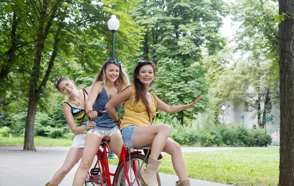 Felice boho chic ragazze cavalcare insieme su biciclette nel parco — Foto Stock