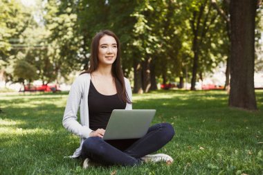 Parkta dizüstü bilgisayar kullanan genç dalgın kadın
