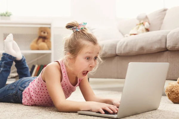 Petite fille décontractée effrayée regardant un film sur un ordinateur portable tout en étant couchée sur le sol à la maison — Photo