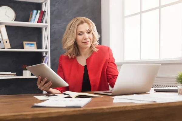 Zufriedene Geschäftsfrau arbeitet am Laptop und hält ein digitales Tablet in der Hand — Stockfoto