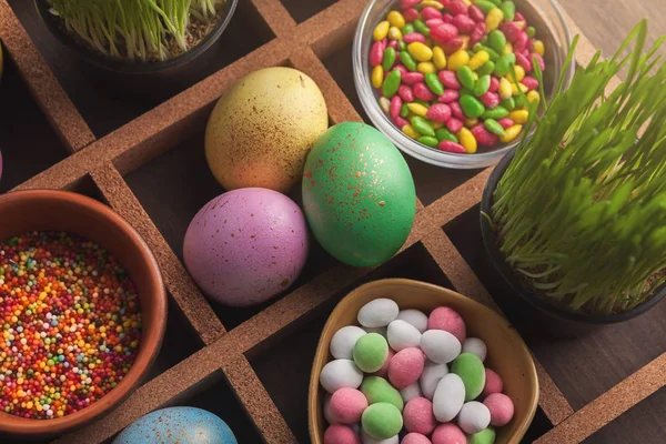 Цветные пасхальные яйца, трава и маленькие конфеты в рамке — стоковое фото