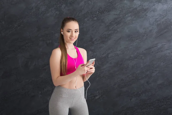 Happy fitness girl in earphones listening music on smartphone — Stock Photo, Image