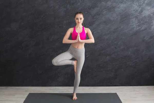 Kvinnan utbildning yoga i tree pose mot grå bakgrund — Stockfoto