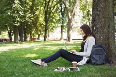 Parkta dizüstü bilgisayar kullanan genç dalgın kadın