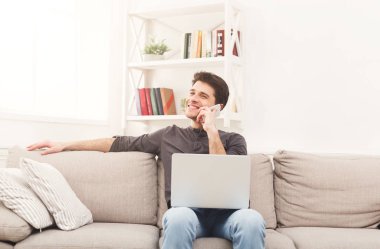 Genç adam evde dizüstü bilgisayar ile ve mobil gülümseyen