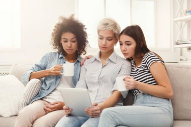 Tablet kullanma ve içme kahve üç mutlu kadın arkadaş