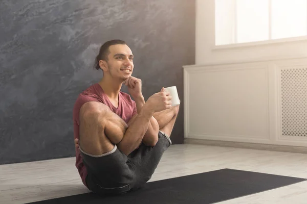 Young man in flexible yoga pose drinking tea