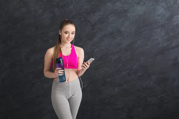 Happy fitness girl listening music on smartphone and drinking water — Stock Photo, Image