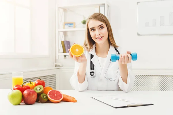 Young dietitian with orange and dumbbell at clinic — Stock Photo, Image