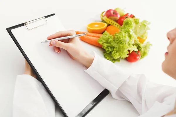 Nutritionist doctor writing diet plan on table — Stock Photo, Image