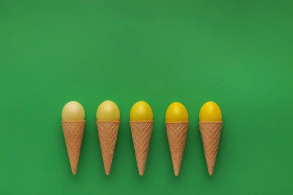 Uova di Pasqua gialle in coni di cialde su sfondo verde — Foto Stock
