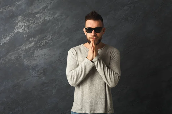 Schöner junger Mann mit Sonnenbrille, der vor grauem Hintergrund betet — Stockfoto