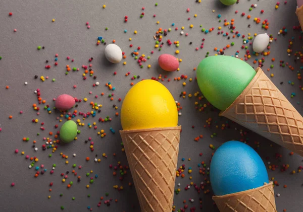 Colorful easter eggs in waffle cones on gray background — Stock Photo, Image