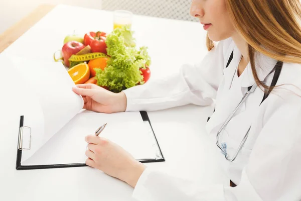 Питательный врач пишет план диеты на столе — стоковое фото
