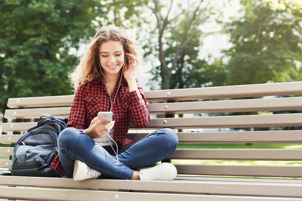 Gyönyörű nő ül és hallgat zenét a smartphone a szabadban — Stock Fotó