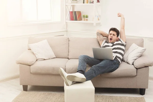 Yawning man using laptop at home