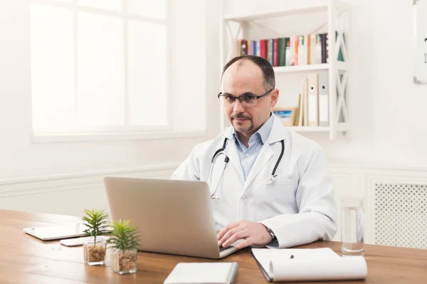 Médico serio en gafas de escribir en el ordenador portátil — Foto de Stock