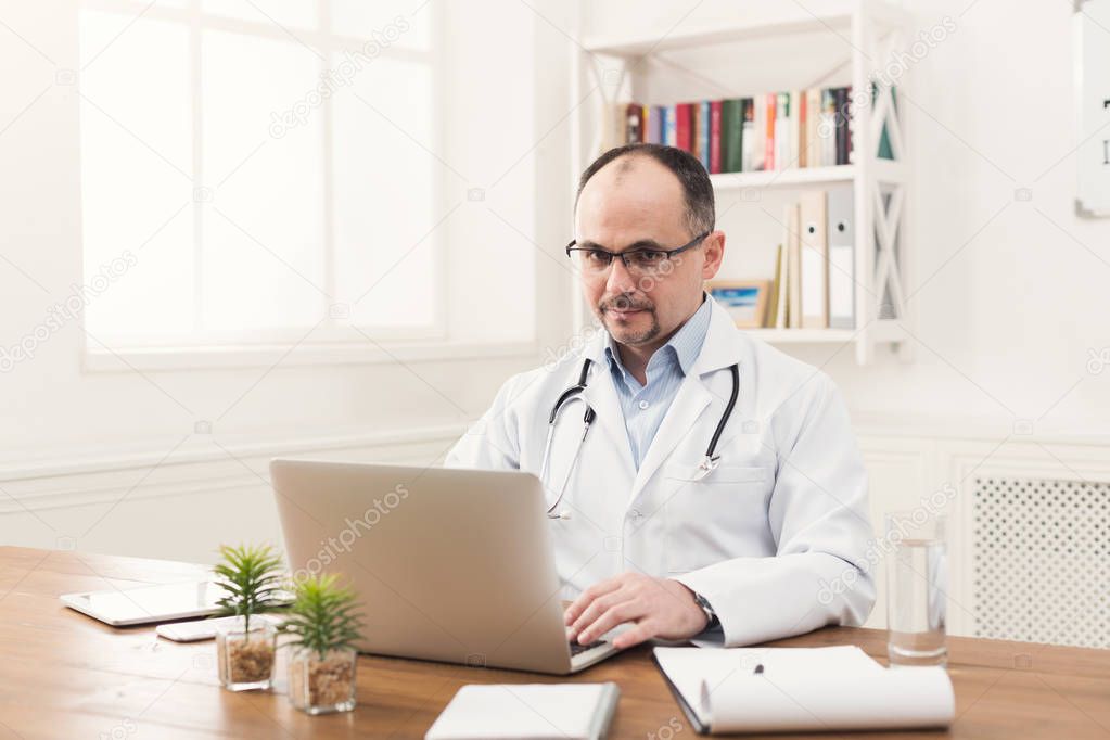 Serious doctor in glasses typing on laptop