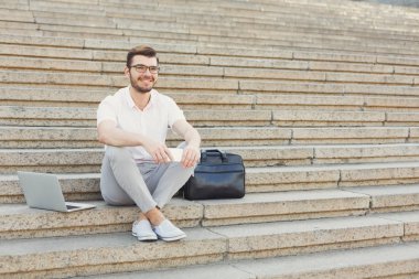 Telefonu ve laptop merdivenlerde kullanarak neşeli genç işadamı