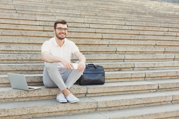 Joven empresario alegre usando el teléfono y el ordenador portátil en las escaleras —  Fotos de Stock