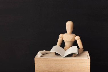 Ahşap şekil siyah arka plan karşı bir kitap okuyor