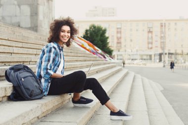 Gülümseyen öğrenci dizüstü kullanarak merdivenlerde oturan