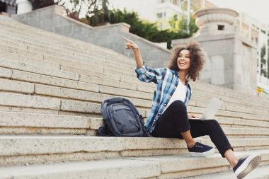 Gülümseyen öğrenci dizüstü kullanarak merdivenlerde oturan