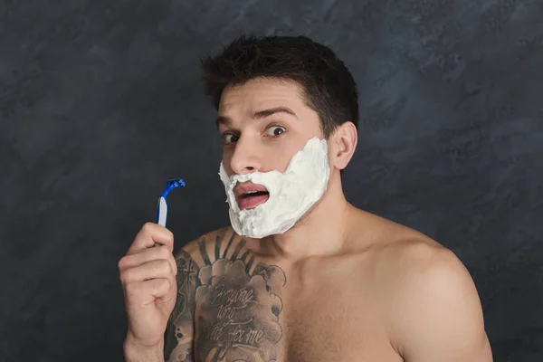 Scared tattooed man with foam on face and razor — Stock Photo, Image