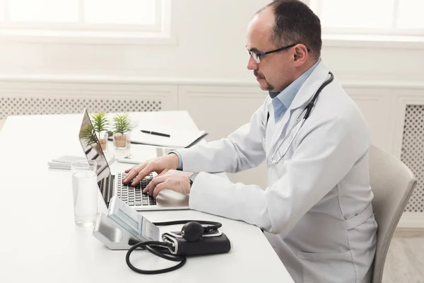 Seriöser Arzt in Brille tippt auf Laptop — Stockfoto