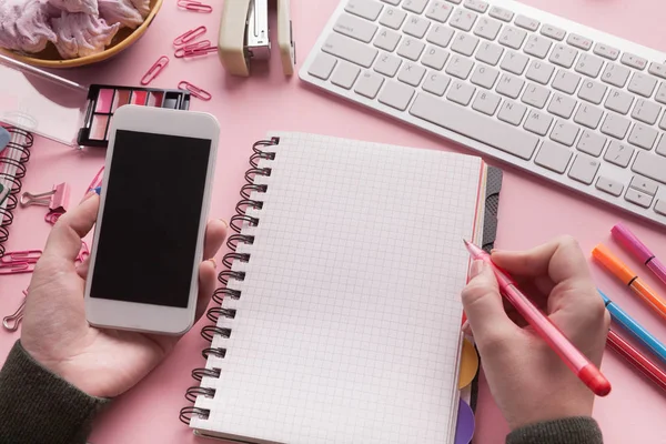 Womans hands holding smartphone and writing in spiral notepad — Stock Photo, Image