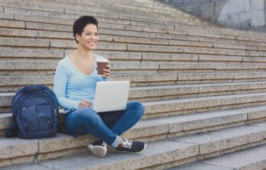 Bir dizüstü bilgisayarda çalışan ve dışarıda kahve içme çekici gülümseyen kadın serbest meslek