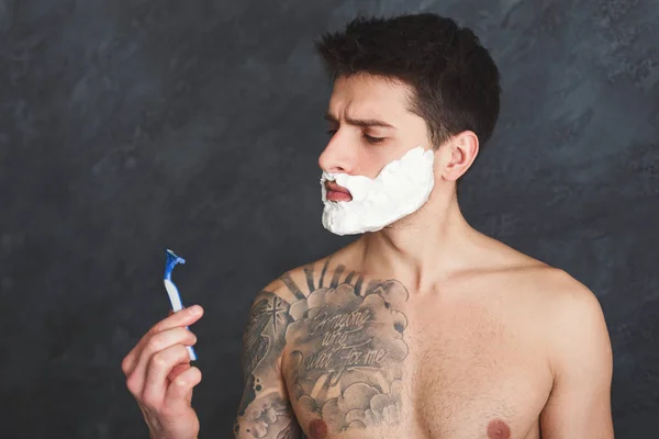 Hombre tatuado asustado con espuma en la cara y maquinilla de afeitar — Foto de Stock
