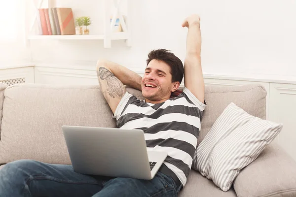 Hombre joven usando el ordenador portátil en casa y estiramiento — Foto de Stock