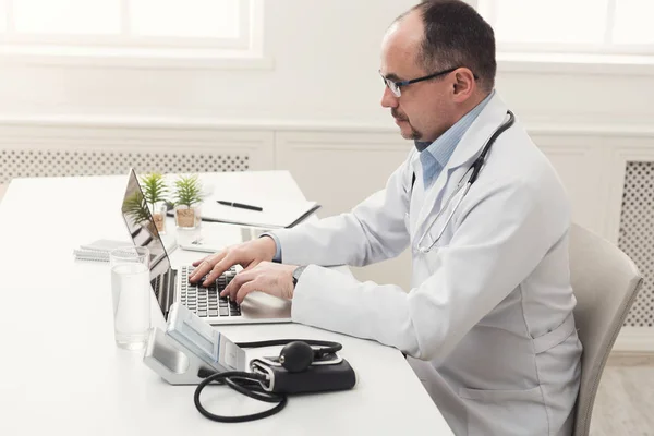 Vážné lékař v brýlích psaní na notebooku — Stock fotografie