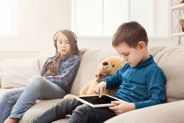 Two kids with gadgets on couch at home — Stock Photo, Image