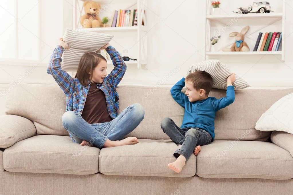 Brother and sister having pillow fight on sofa