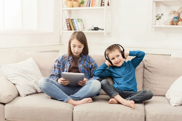 Двое детей слушают музыку дома на диване — стоковое фото