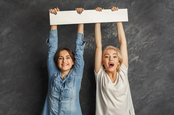 Ragazze felici con banner bianco vuoto su sfondo scuro studio — Foto Stock