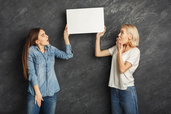 Meninas chocadas com banner branco em branco no fundo do estúdio escuro — Fotografia de Stock